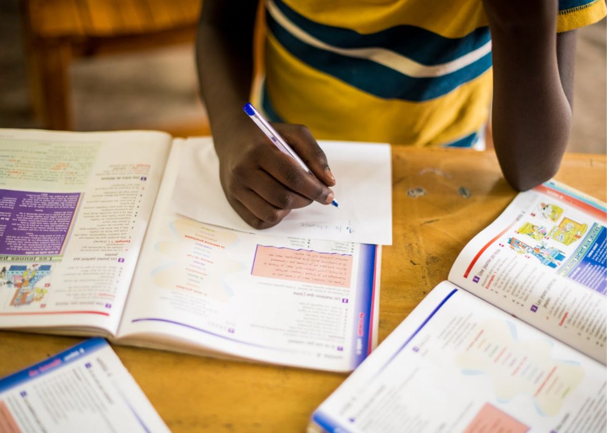 A student writing at a desk with open workbooks